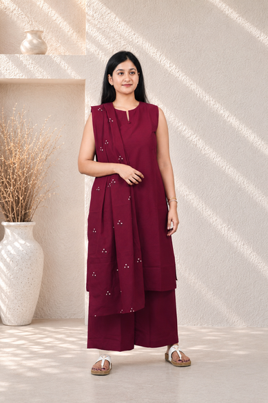 Woman wearing a maroon outfit with a white vase and decorative branches in the background
