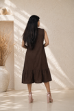 Woman wearing a brown dress standing in a sunlit room with a textured wall.