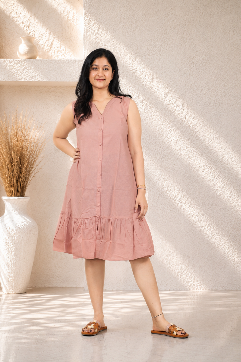 Woman wearing a pink dress standing in a softly lit room with a vase and plant in the background.