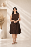 Woman wearing a brown dress standing in a softly lit room with decorative elements.
