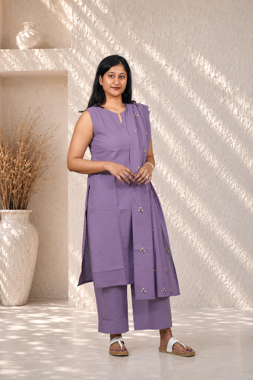 Woman wearing a purple outfit standing in a well-lit room with a decorative vase and plant.